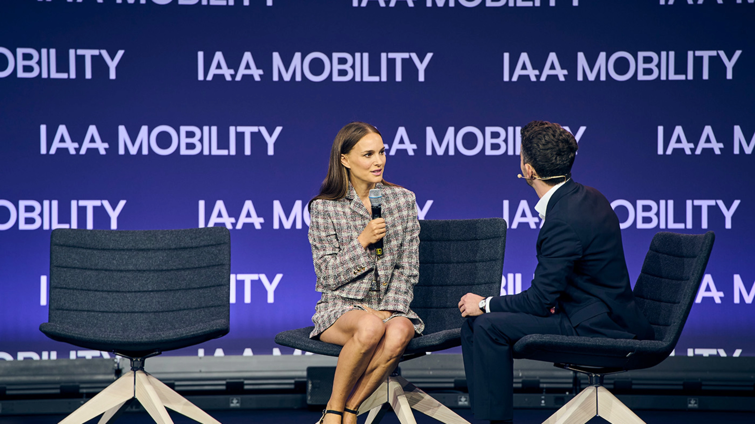 Natalie Portman in a live on-stage interview at IAA Mobility, seated next to a moderator, with a backdrop displaying the event logo.